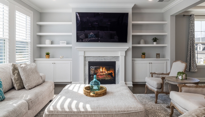 A white living room with cream colored furniture and a fireplace focal point.