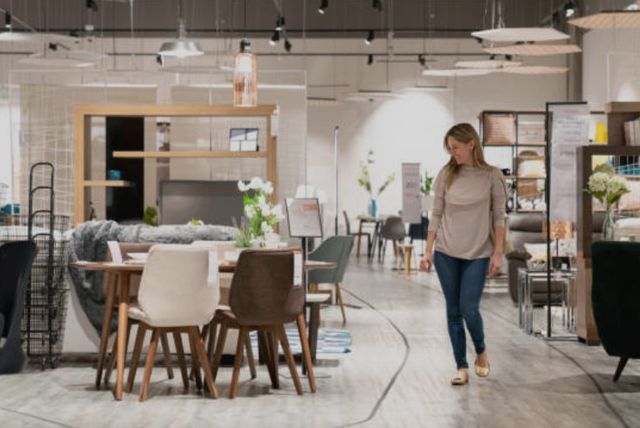 front view of a woman walking through a furniture store looking at a dining table and chairs smiling