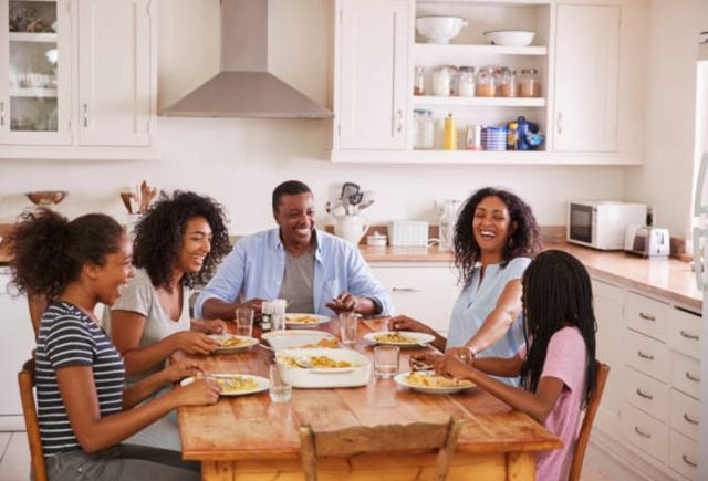 front view of a family smiling and laughing at a wooden rectangular dinner table with food in front of them