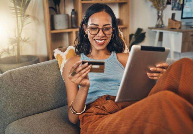 front view of a woman sitting on a sofa smiling while shopping on her iPad