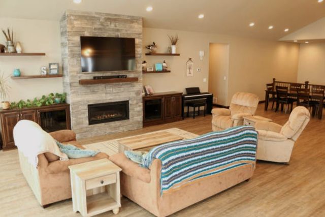 view of a modern living room with a tv above the fireplace, surrounded by a couch, loveseat, and two recliners