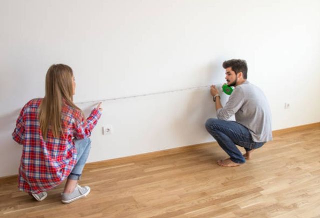 front view of two people kneeling down and holding a measuring tape from either end against a wall