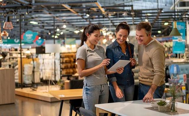 front view of a saleswoman and a couple all looking at a tablet in a furniture store