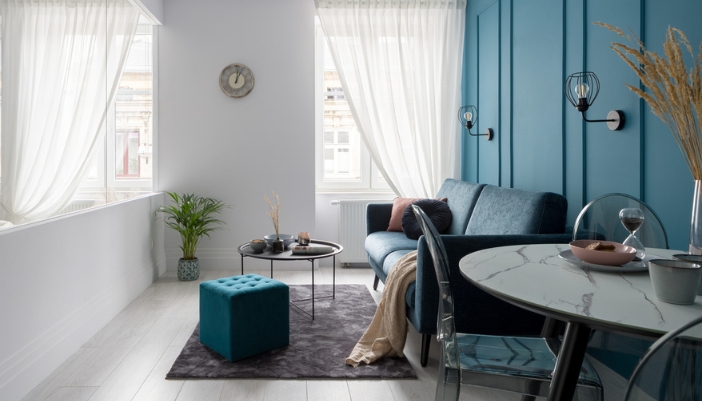 A living room with a blue accent wall and some navy furniture and wispy curtains.