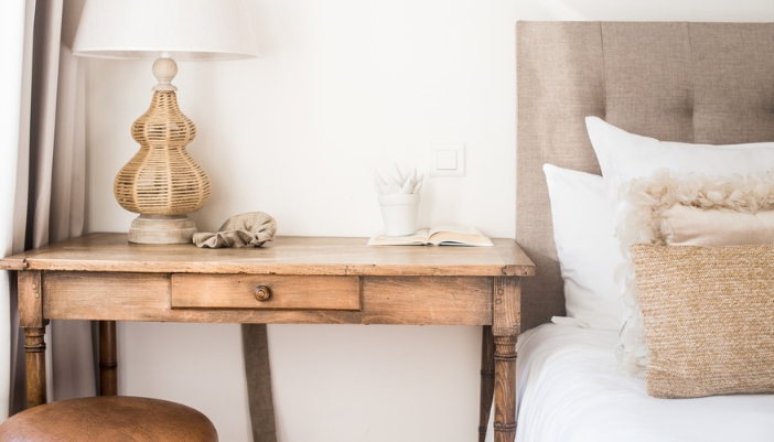 A natural wooden side table next to a made bed in bedroom.