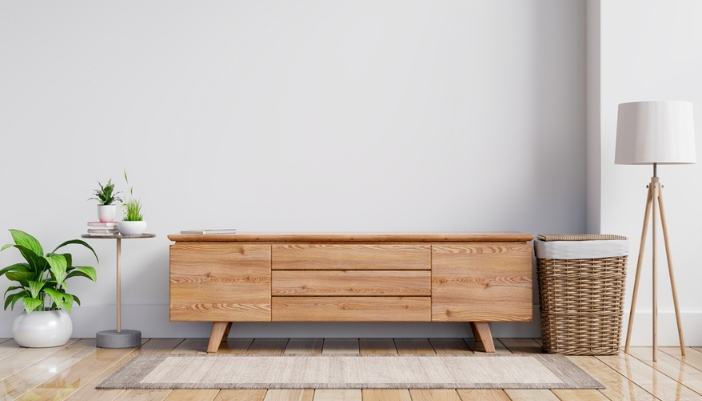 A wooden console table rests between a basket and plants before a neutral wall.