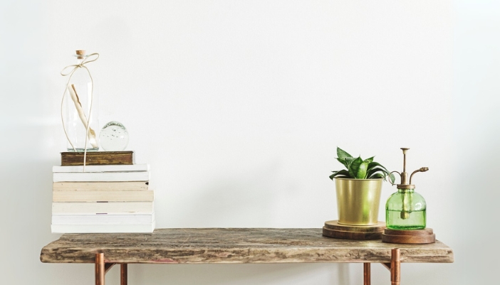 A wooden and copper slim table with plants and a watering can on top.
