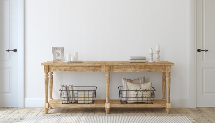 A wooden slim table in a home’s entryway with candles on top and baskets with pillows.