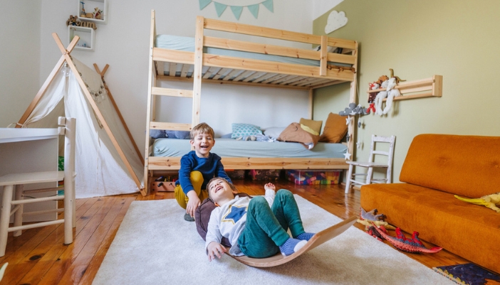 Two small boys play with a teeter totter in their bedroom.