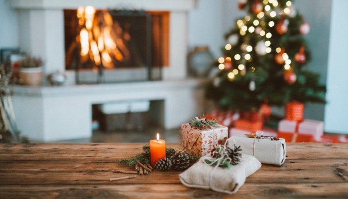 A lit candle rests next to wrapped gifts in a room decorated for the holidays.