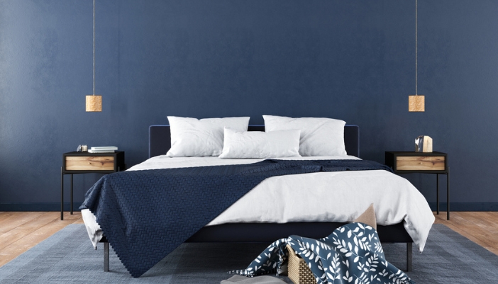 A white bed sits in front of a navy blue accent wall.