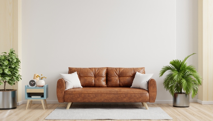 A brown leather couch and retro furnishings sits in front of a neutral colored wall. 