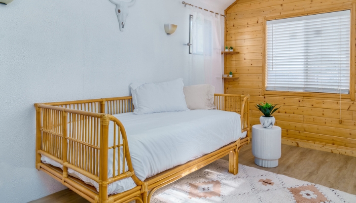 A natural wooden day bed with white sheets sits in a boho type room.