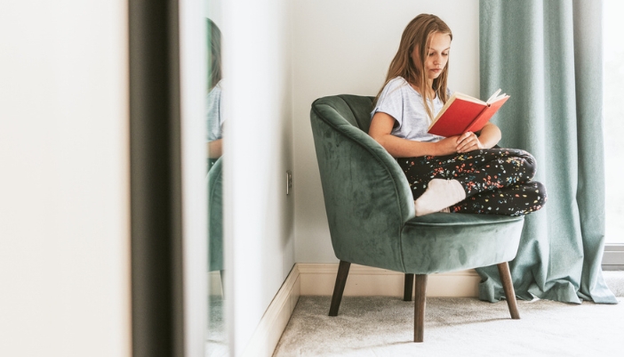  young female child sits in a green velvet chair reading at home.
