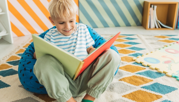 A young boy sits in a bean bag chair reading a book.