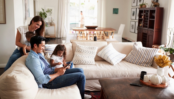 A family sits together on a white sectional in their living room.