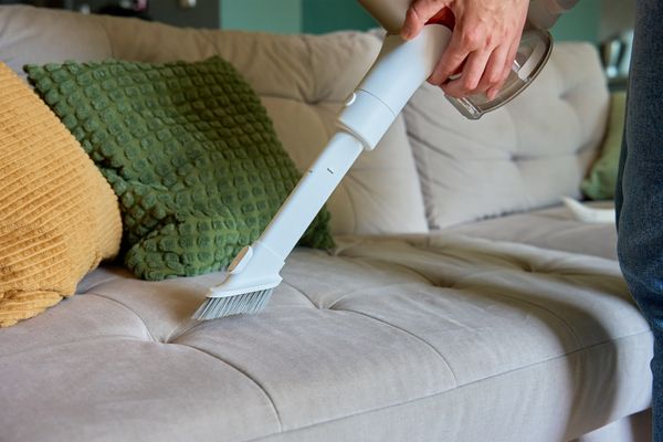 A person vacuuming a grey microfiber sofa 