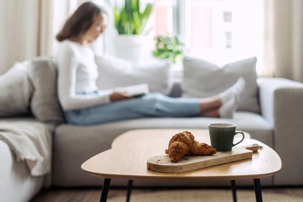 A wooden coffee table with pastries in the foreground and a woman reading in the background 