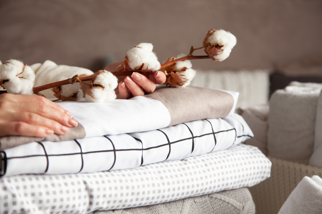 female hands holding the cotton branch with pile of folded bed sheets and blankets