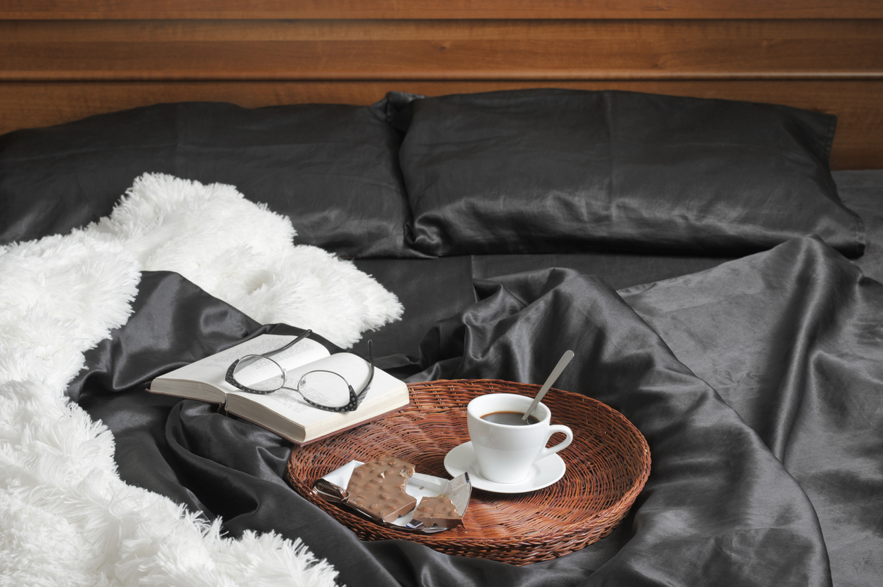tray of coffee with chocolate and book on silk bed sheets