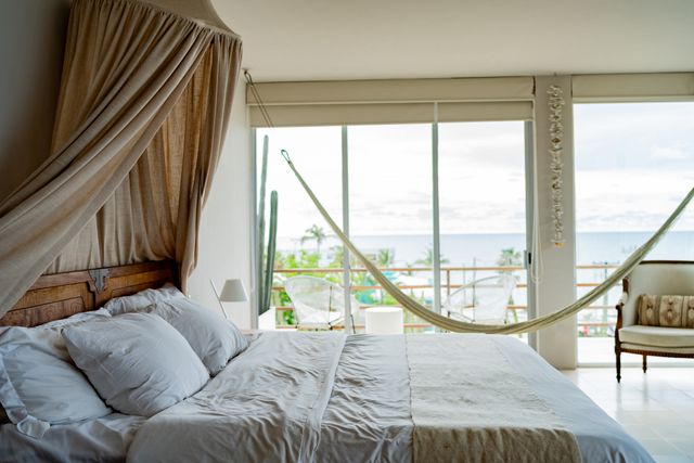 Front view of a modern coastal bedroom with light walls and breezy light blankets on the bed and around the room
