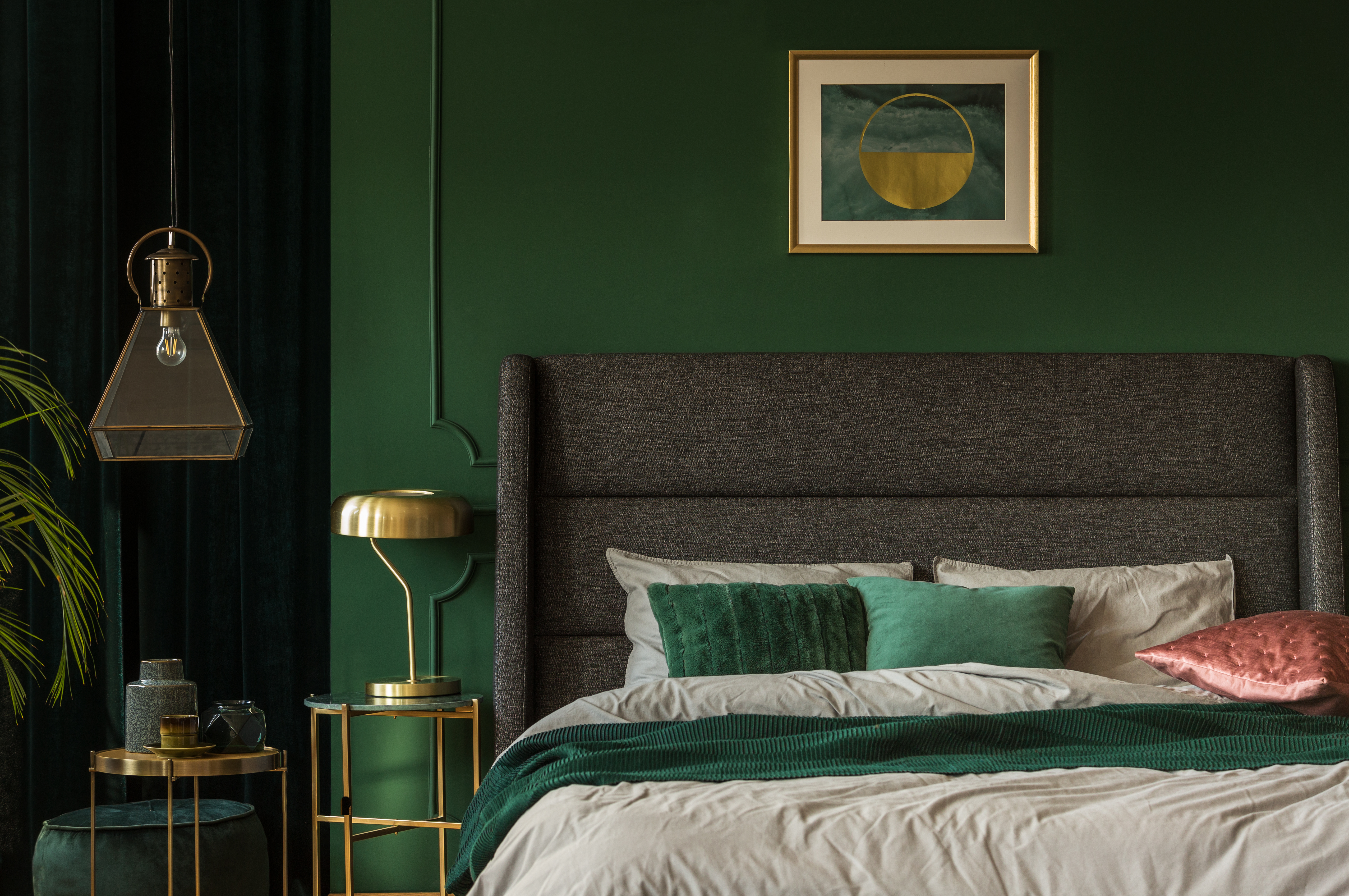 A grey upholstered headboard featured against a green wall with green bedding 