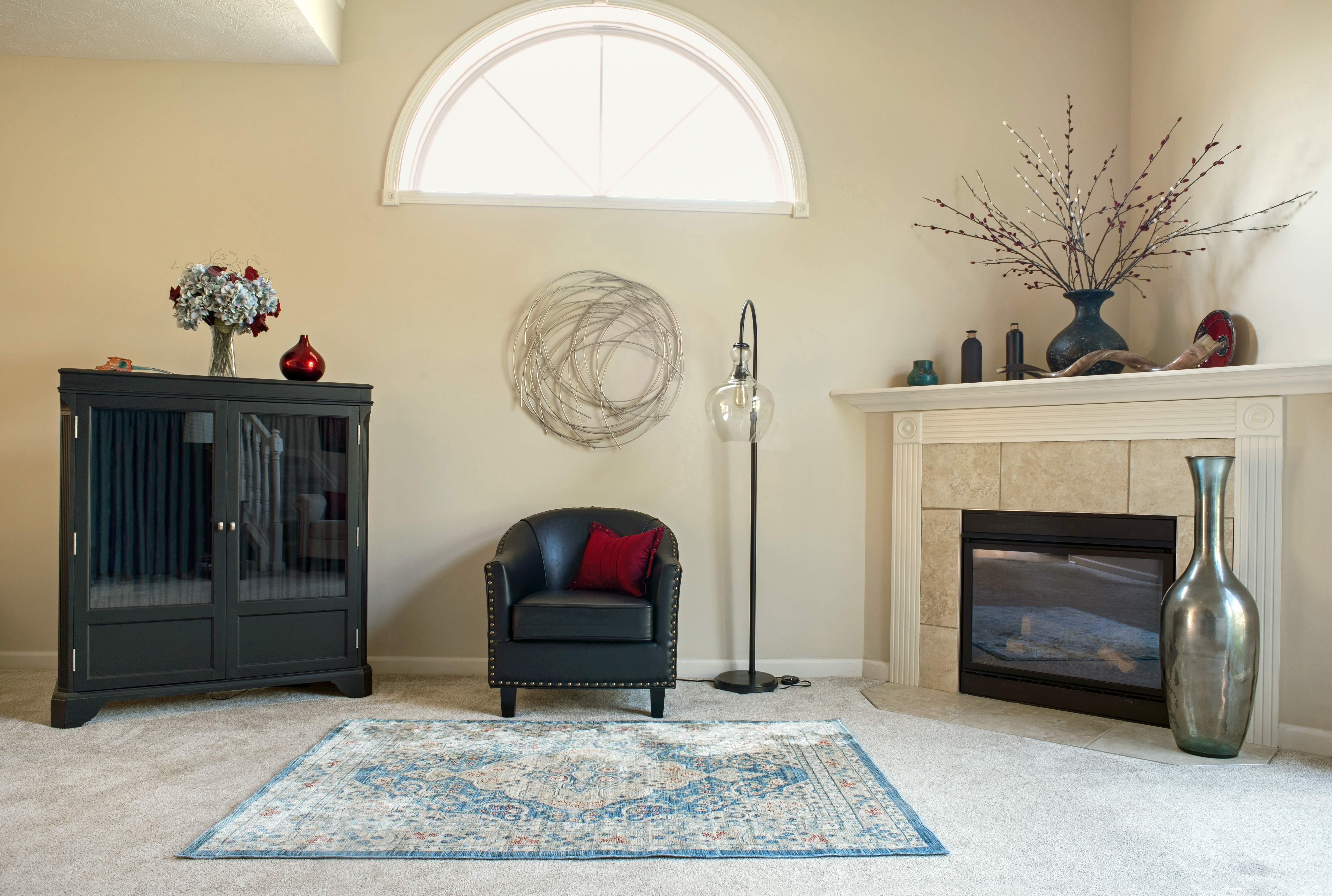 A living room featuring a corner fireplace, black accent chair, blue rug, and metallic vase 