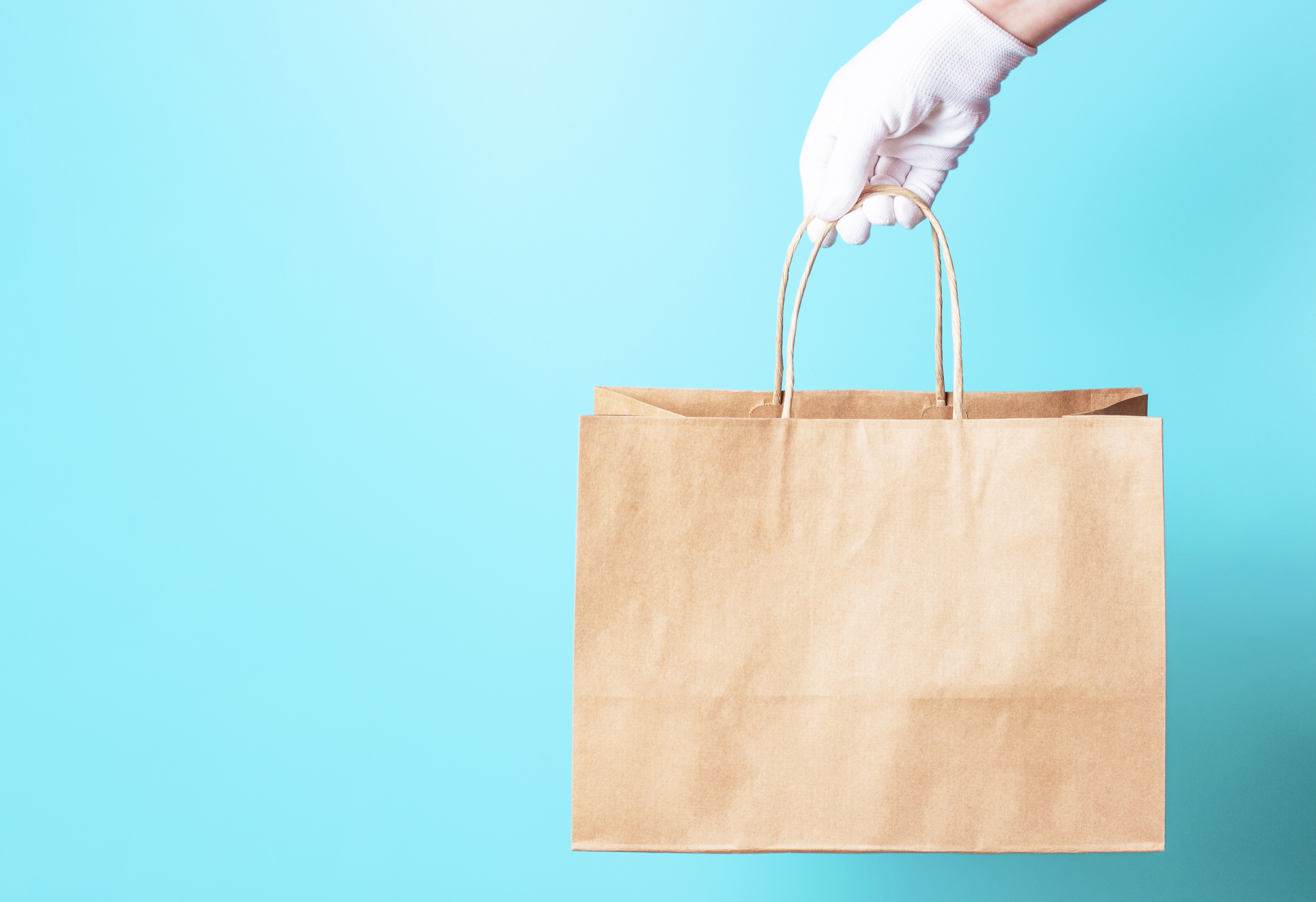 Person wearing a white glove delivering a bag in front of a blue background 