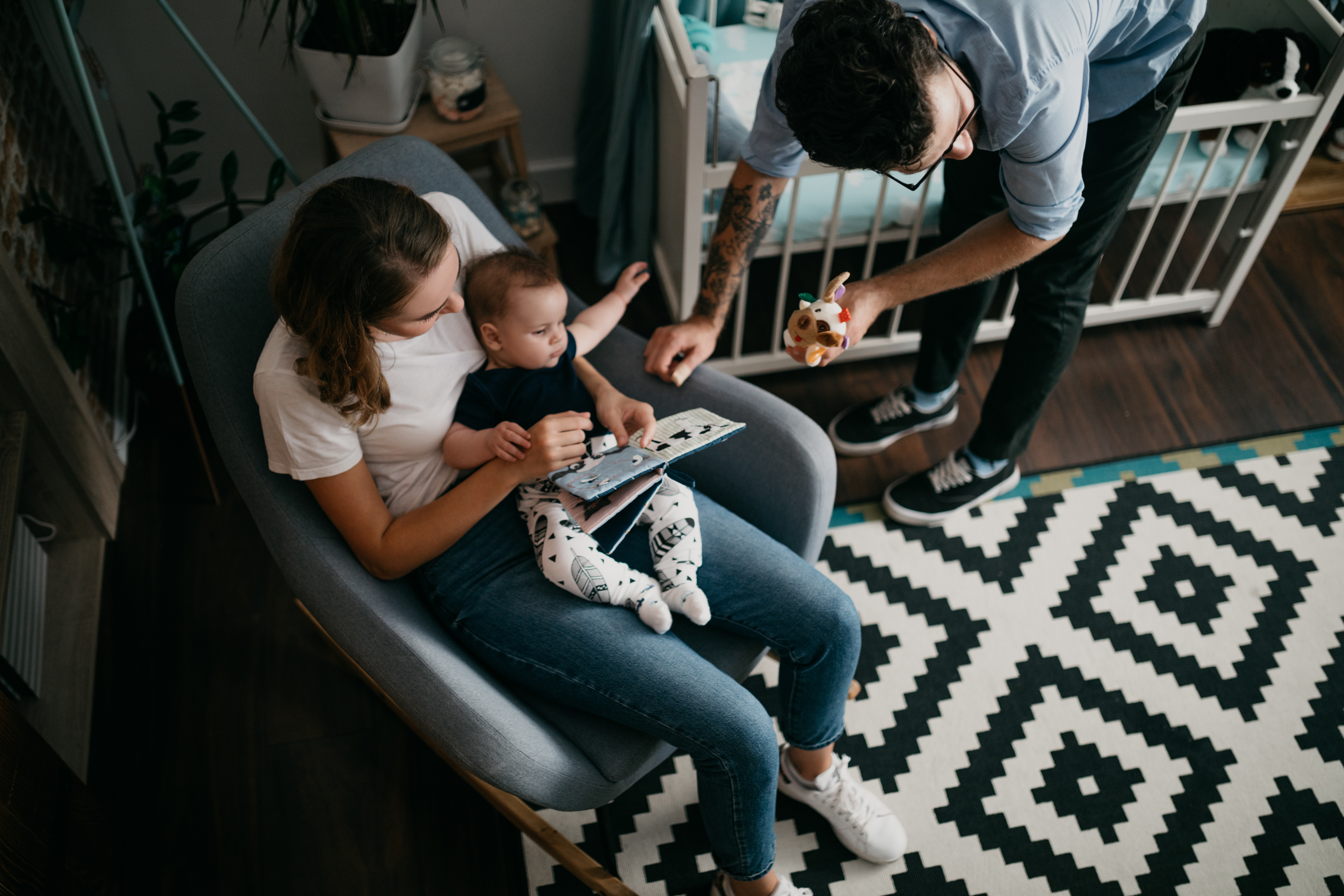 A woman holds a child in a rocking chair while a father holds a toy on the side 
