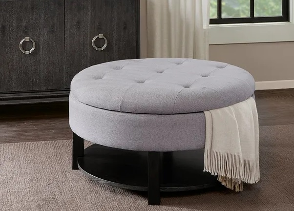 Madison Park Ollix round storage ottoman with tufting, grey upholstery, open bottom storage, and a throw