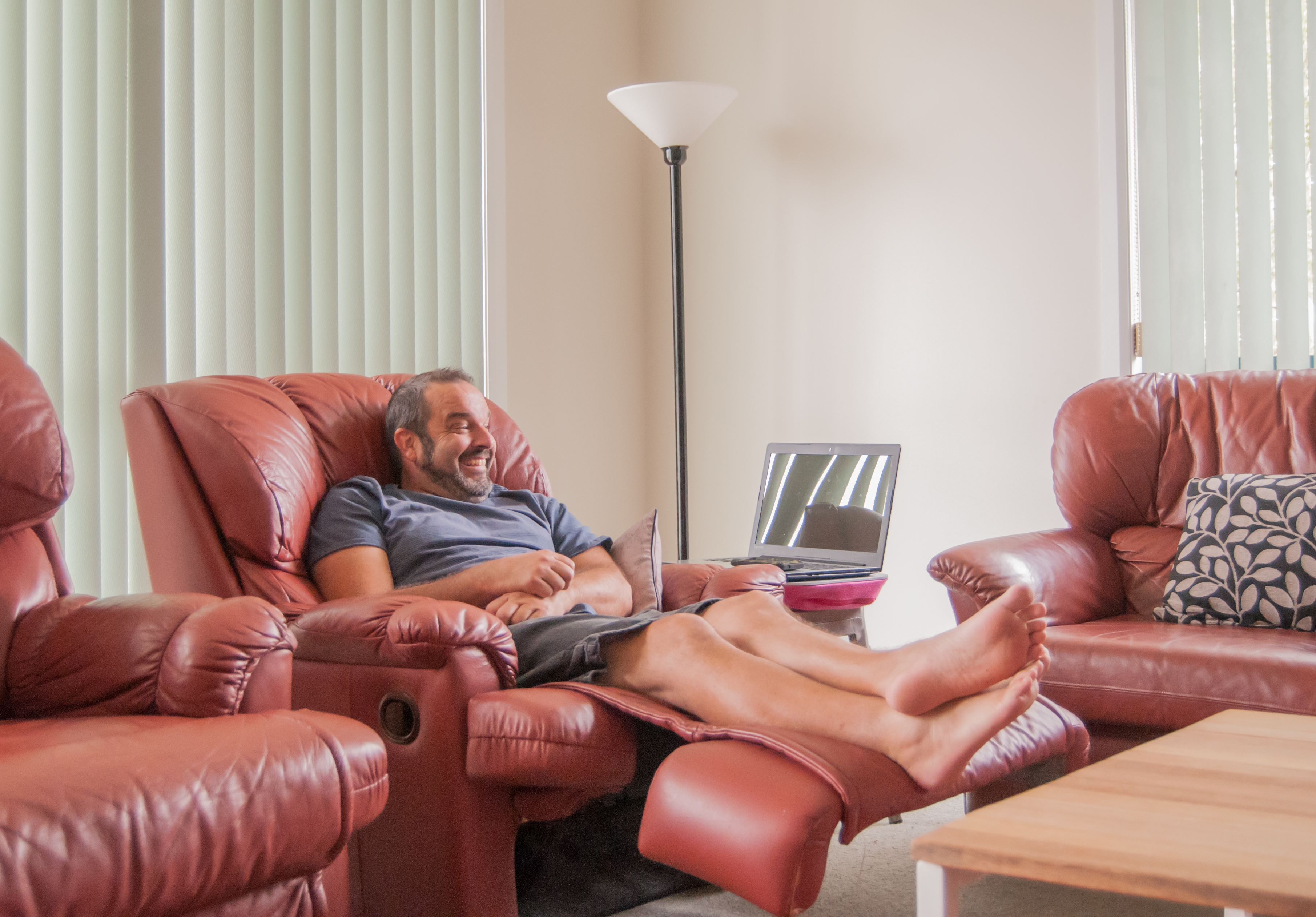 Man seated in a red faux leather recliner with a laptop 