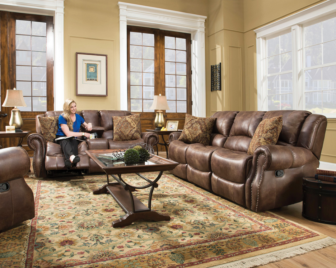 Woman shown sitting on a traditional style leather living room loveseat with matching sofa and chair 