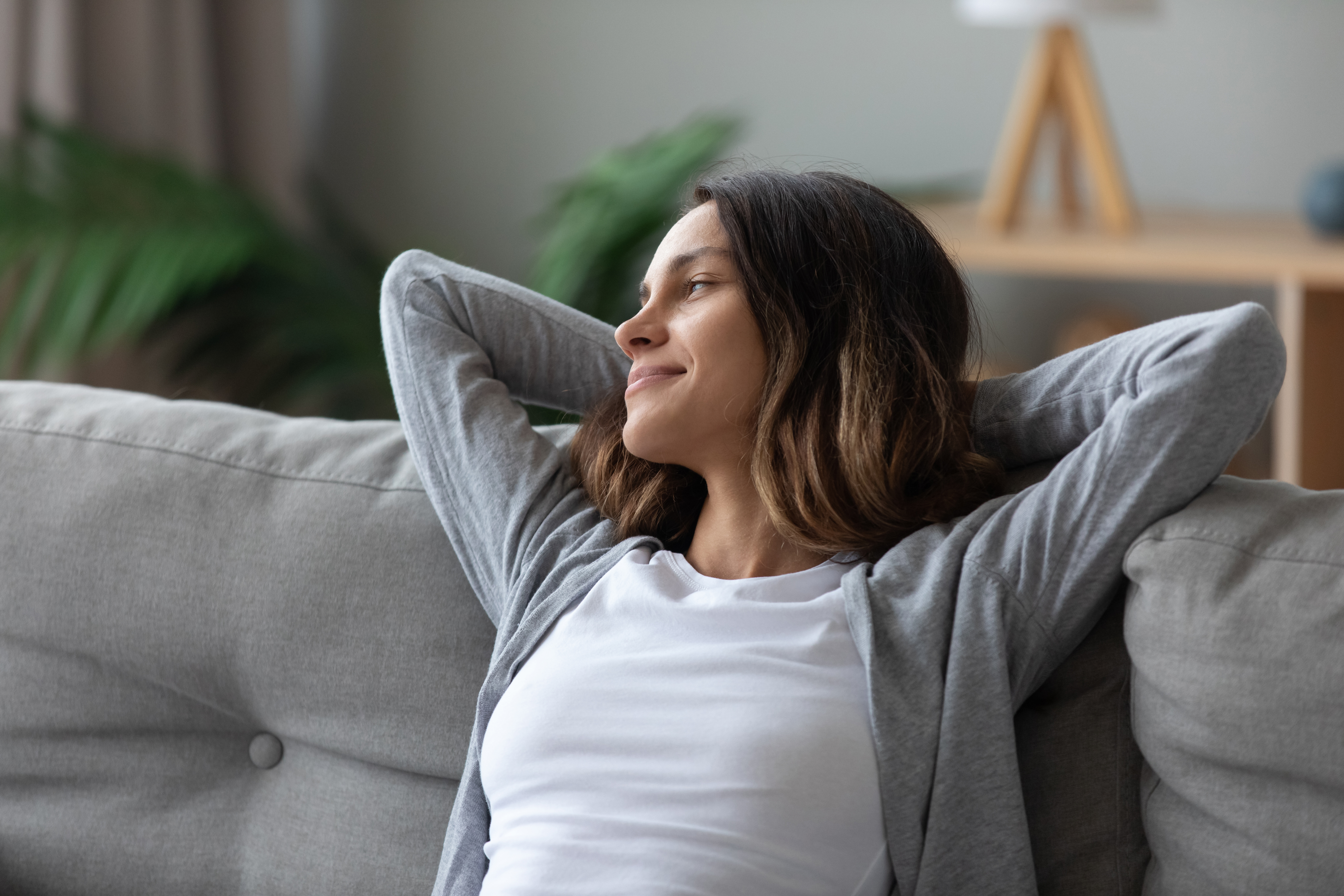 Woman with her arms crossed behind her head smiling as she sits on a sofa 