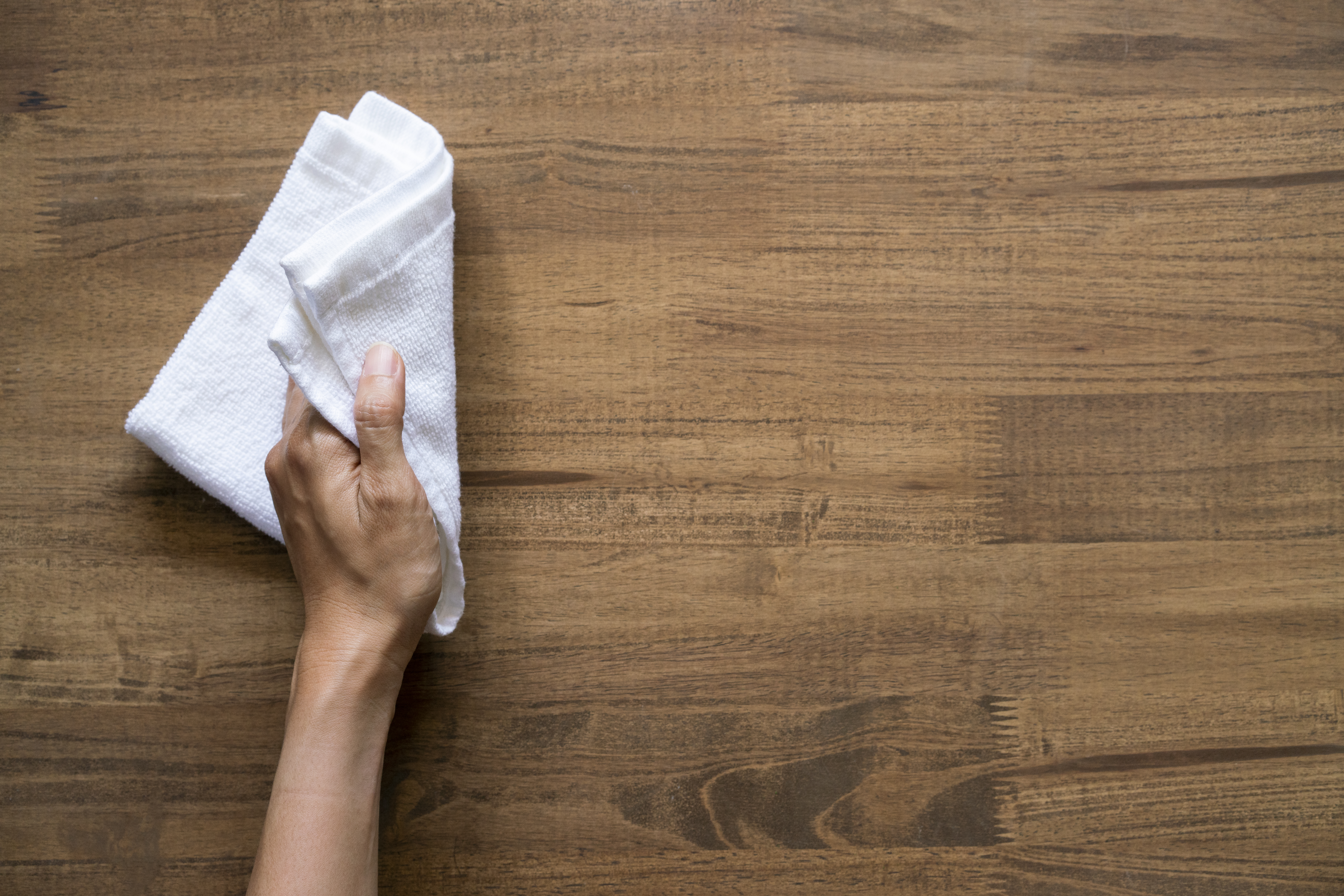 Person using a white cloth to clean a wooden surface 