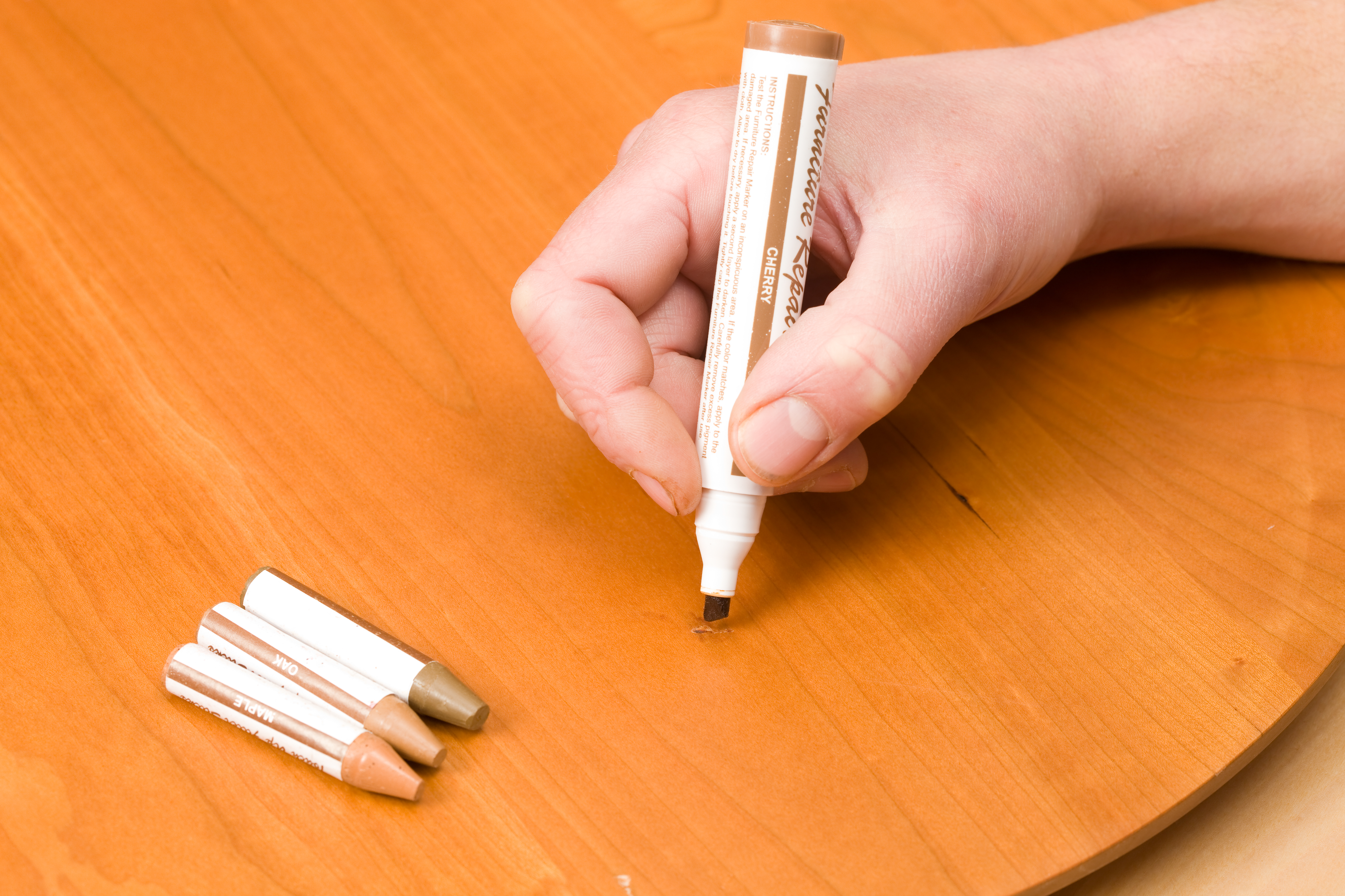 Person using a wood repair pen on a wooden surface 