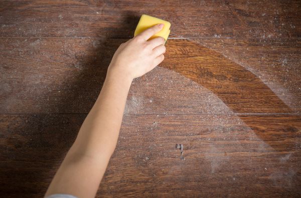 person's arm using a sponge to clean dust from a wood dining table