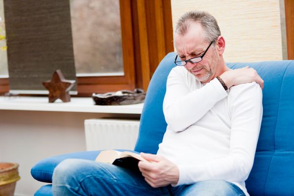 A man wincing in pain while reading on a blue chair