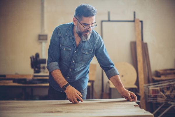 A man in a denim shirt measuring a slab of wood 