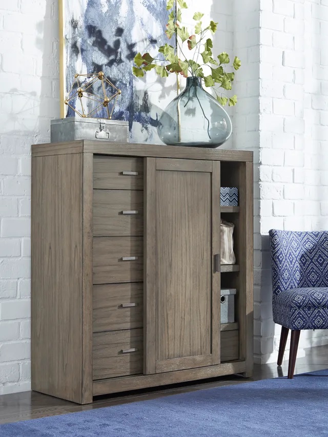 Wooden slide door Aspenhome dresser sitting in a modern bedroom displaying a green plant on top. 