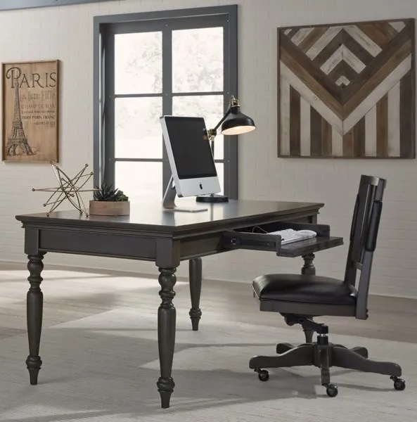 A modern home office with artwork on the walls, a wooden desk, and a computer and lamp sitting on top. 
