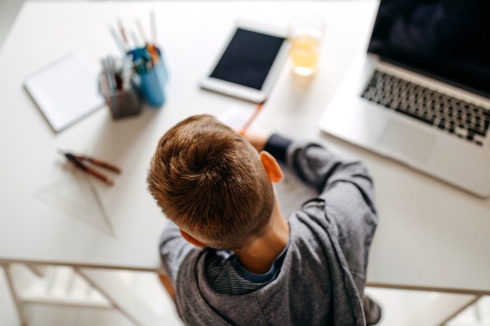 Young boy sitting in his room and doing homework on a desk for kids. 