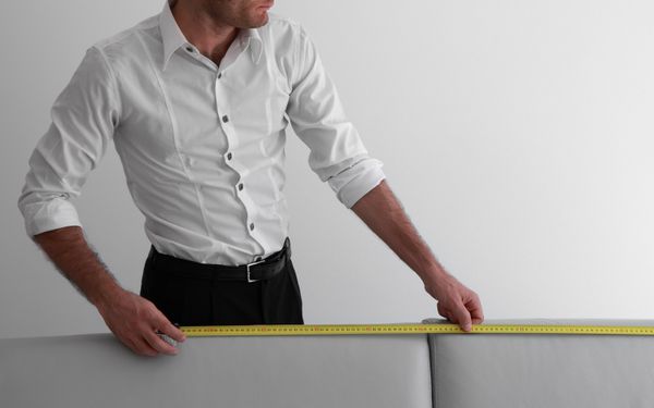 A man in a white button-up measuring a sofa 
