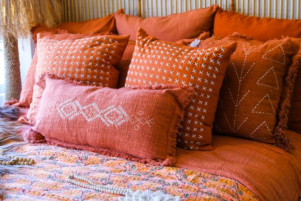 A bed featuring various orange-tone pillows of different sizes and patterns 