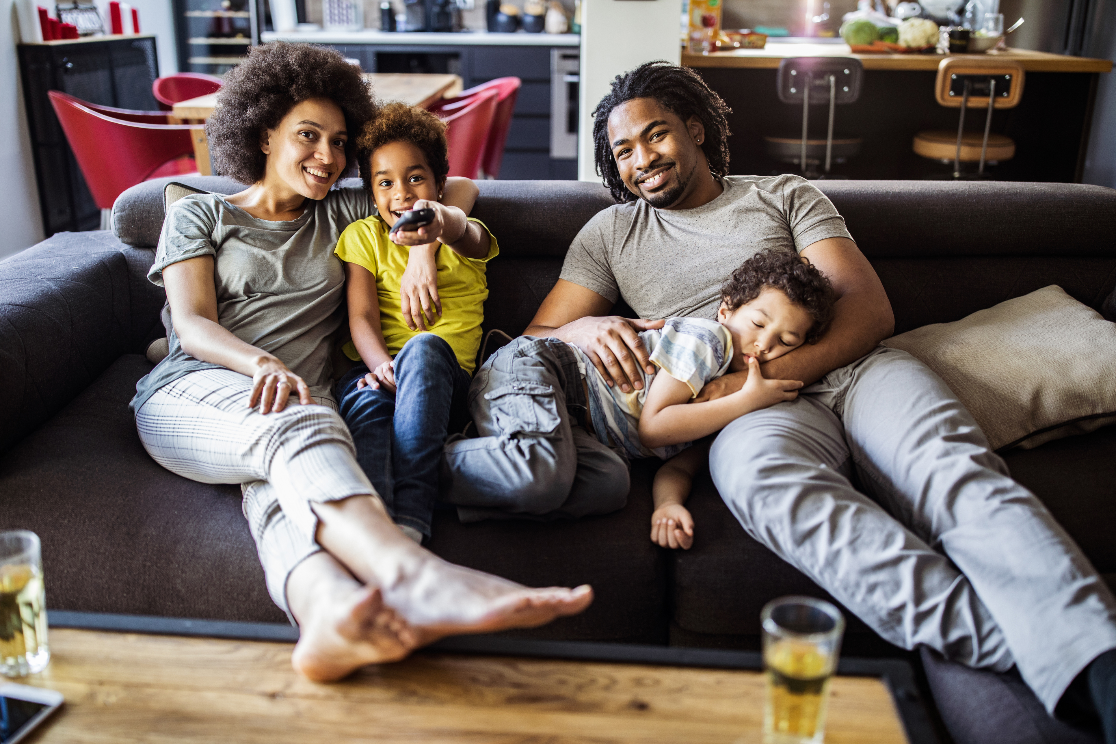 A family of four sitting and smiling while watching TV 