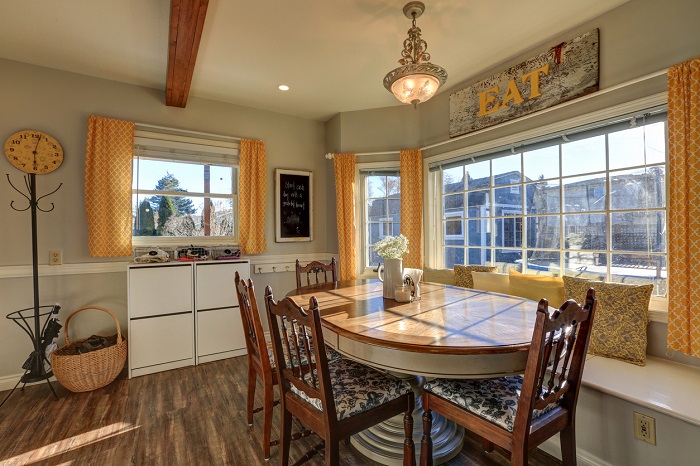 Sun filled farmhouse breakfast nook showcases oval table with carved chairs and cozy window seat. 