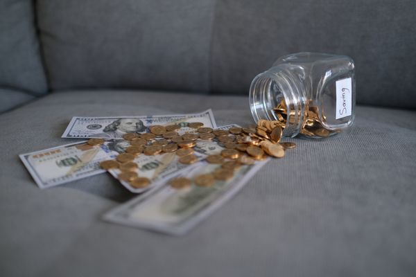  A jar with spilled $100 bills and pennies on a sofa