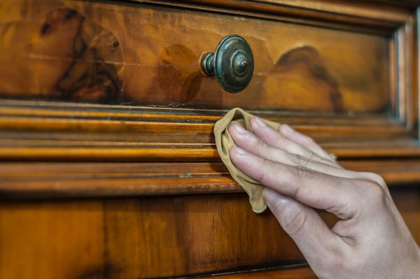 A person buffing a wooden dresser 