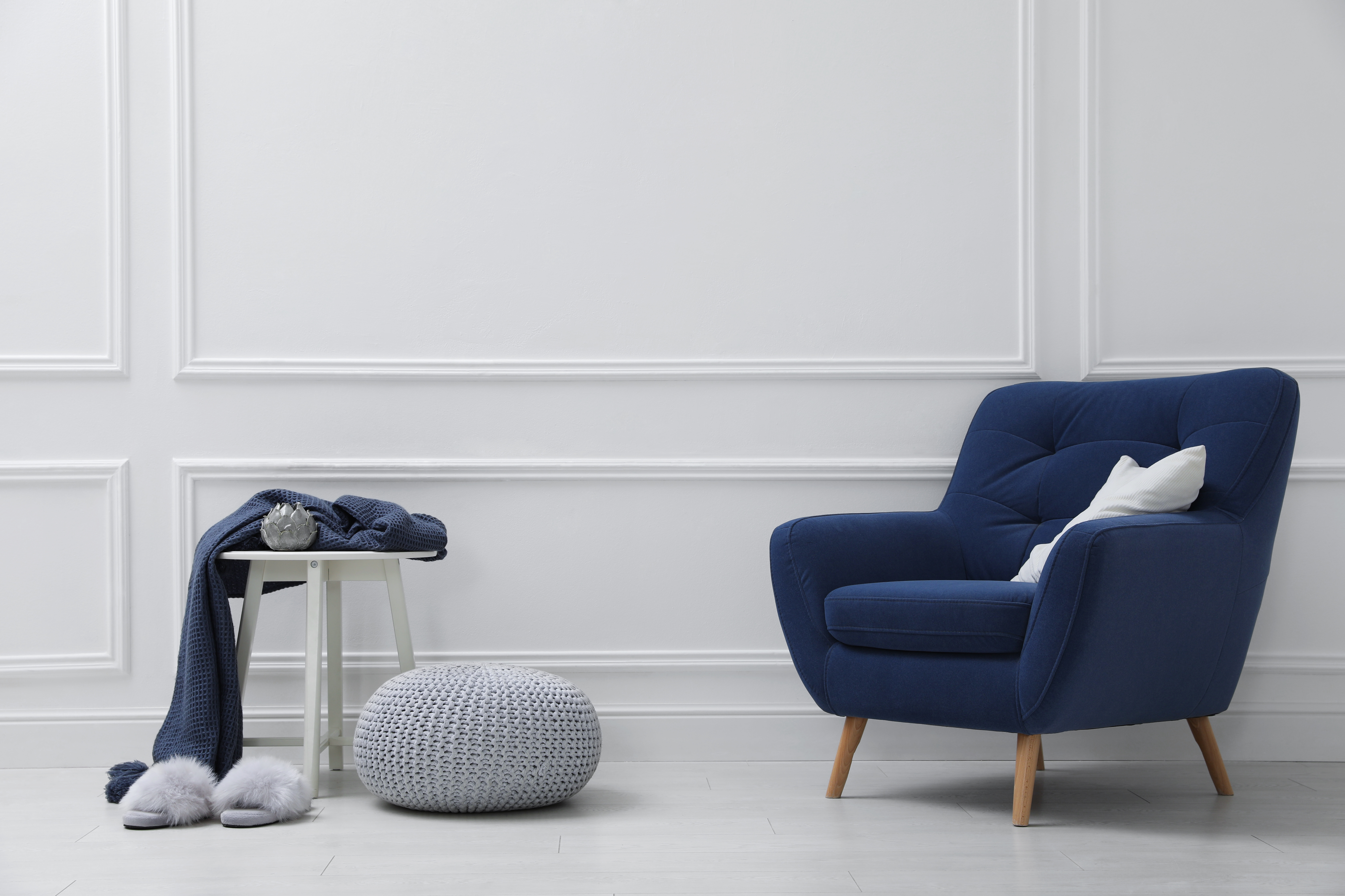 Grey knitted pouf next to a blue armchair 
