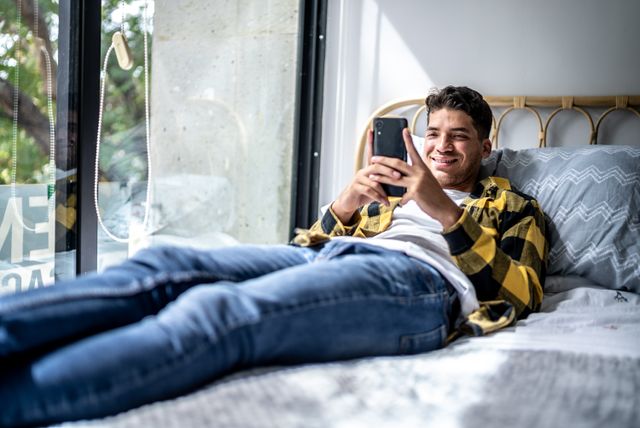 A young man in yellow and black flannel smiling on a rattan bed 