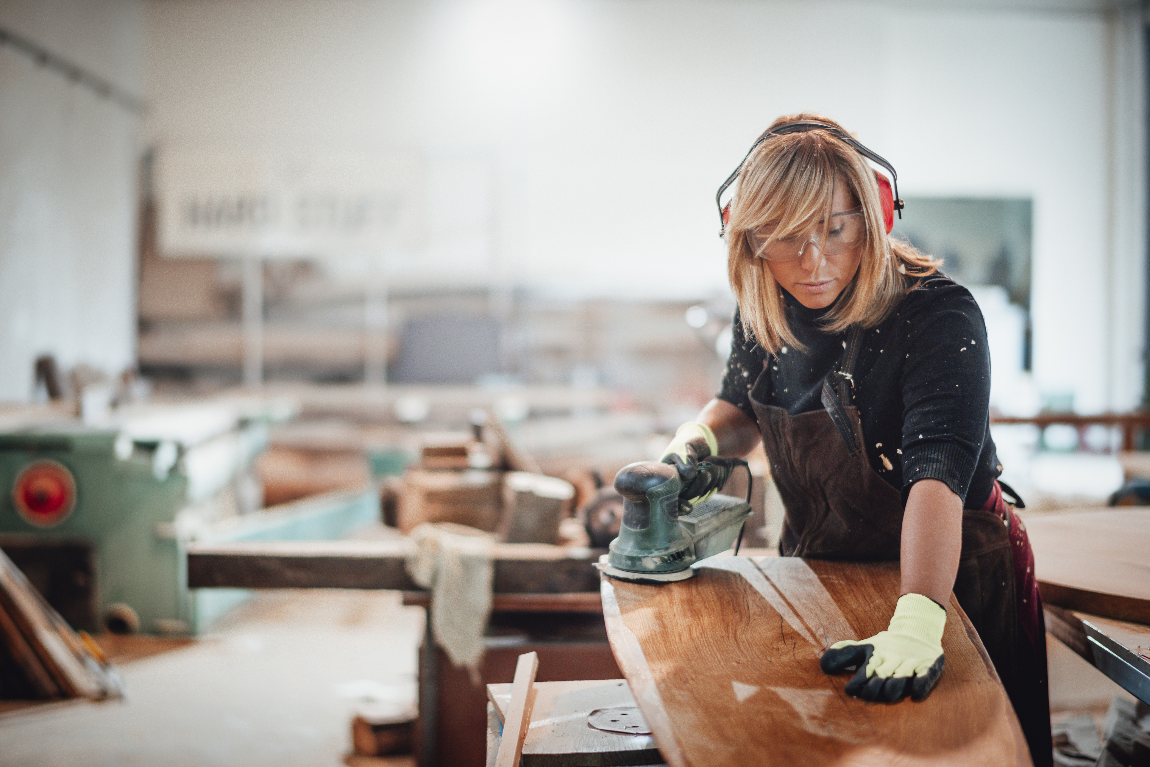 A woman sanding down a plank of solid wood 